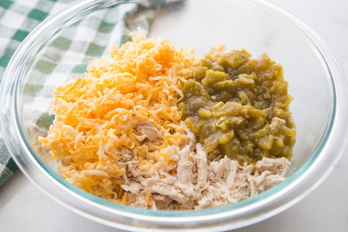 Ingredients for chicken enchiladas - Chicken, cheese, and green chilies mixed in a glass bowl.