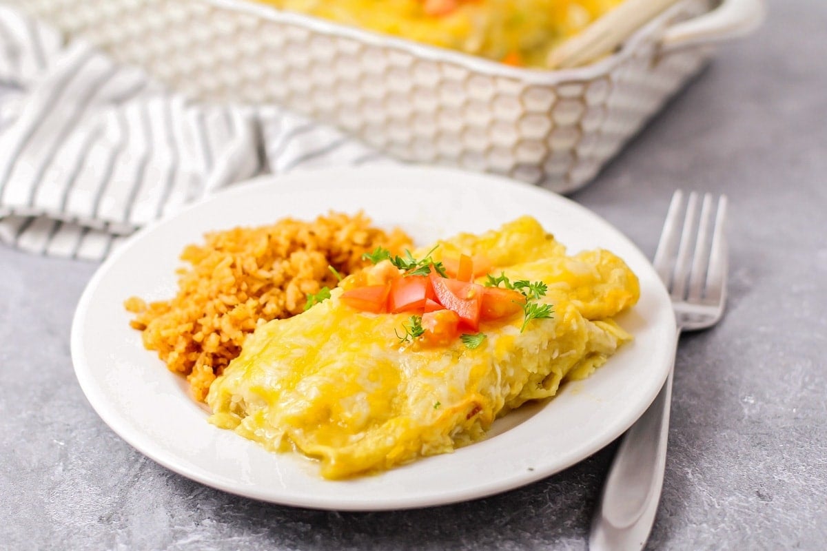 Green Chili Chicken Enchiladas served on a plate and topped with tomatoes.