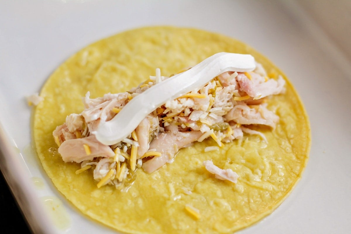 A corn tortilla topped with a chicken mixture and a line of sour cream.