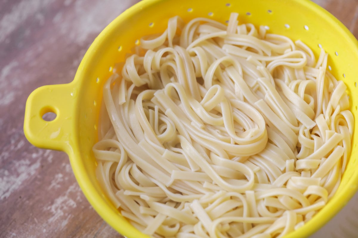 Fettuccine Noodles draining in a yellow colander for making Fettuccine Alfredo.