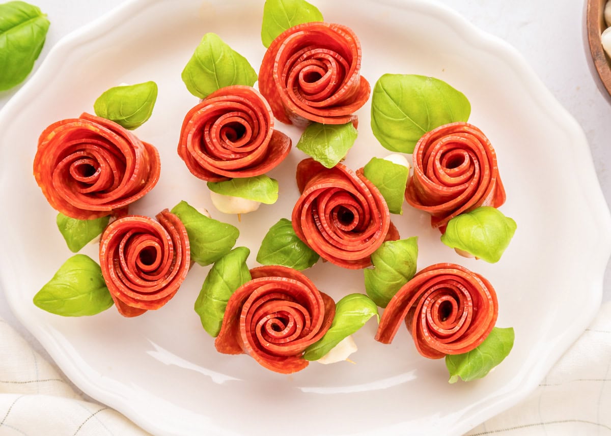 Several pepperoni rose skewers on a white serving platter.