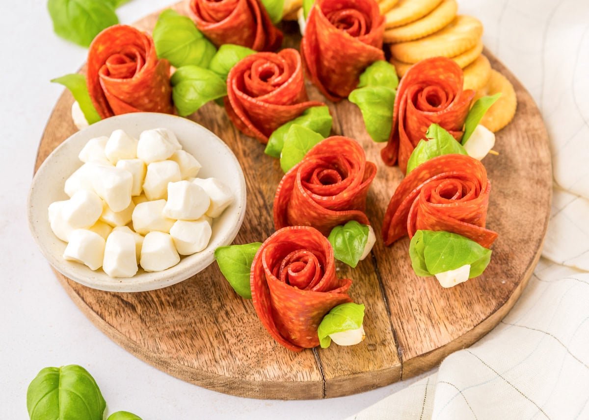 A wooden board topped with pepperoni rose skewers.