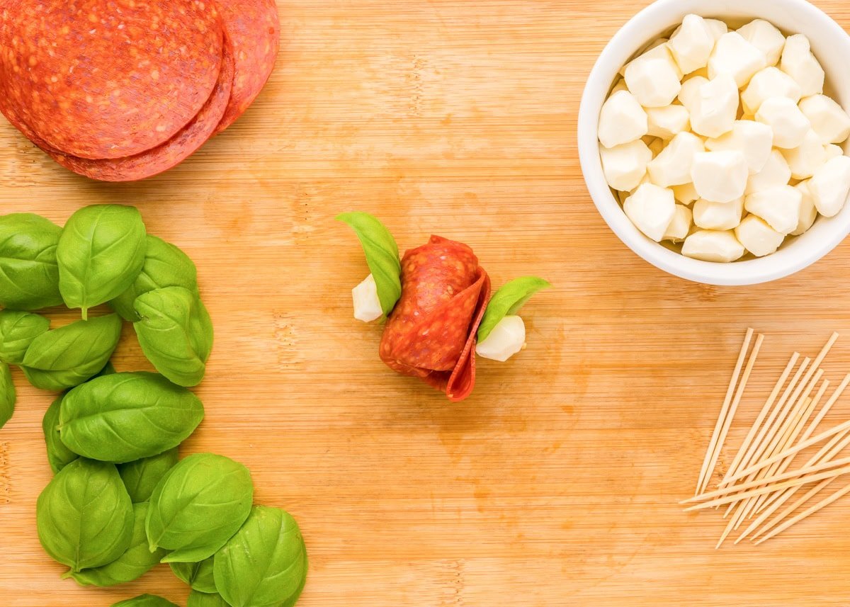 Adding mozzarella and basil to the skewers.