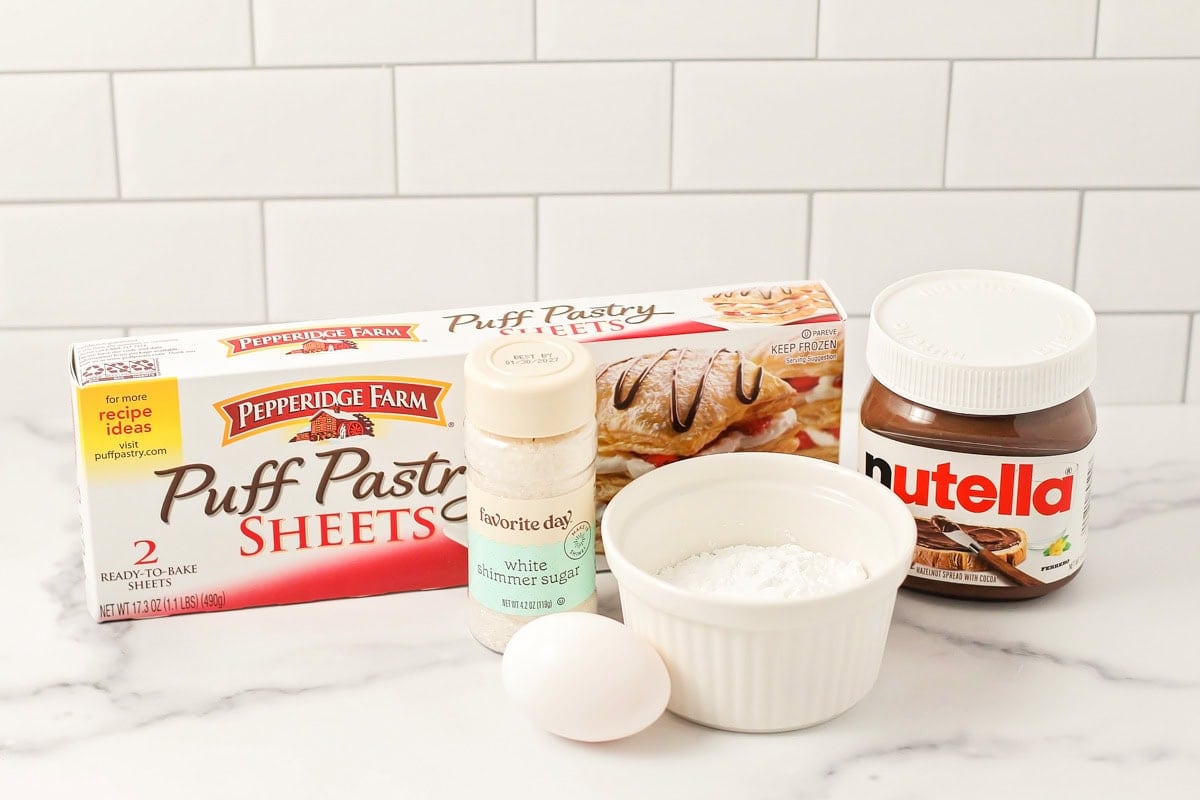 Puff pastry, Nutella, powdered sugar, and egg on a kitchen counter.